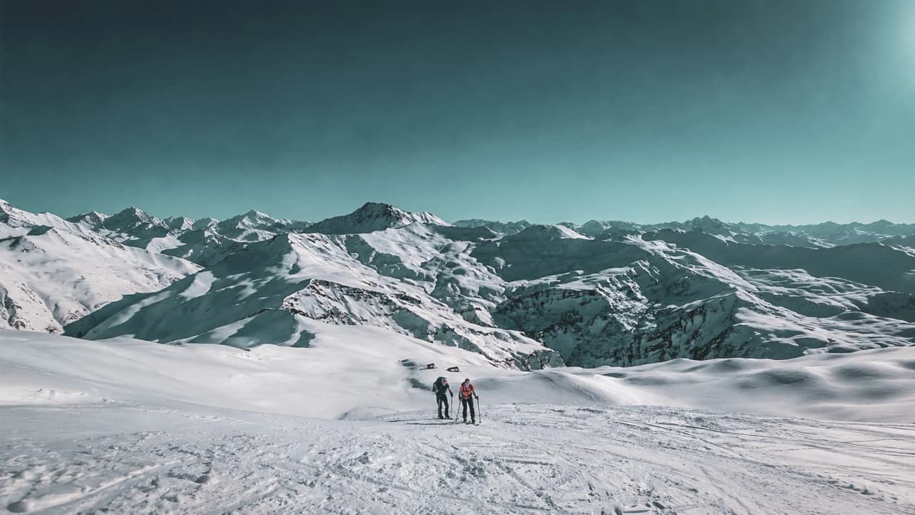 Two cross-country skiers in a vast snowy landscape, with mountains stretching as far as the eye can see.