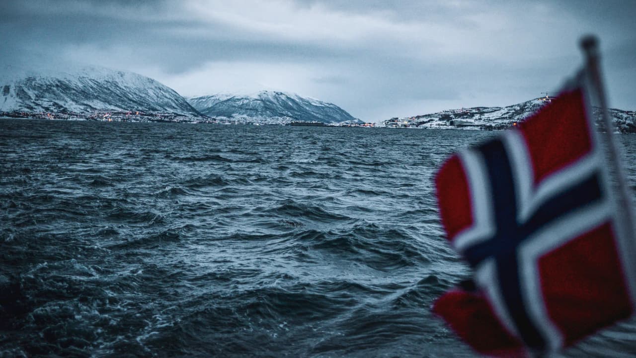 A view of the fjords of Tromsø with snow-capped mountains and a Norwegian flag flying.
