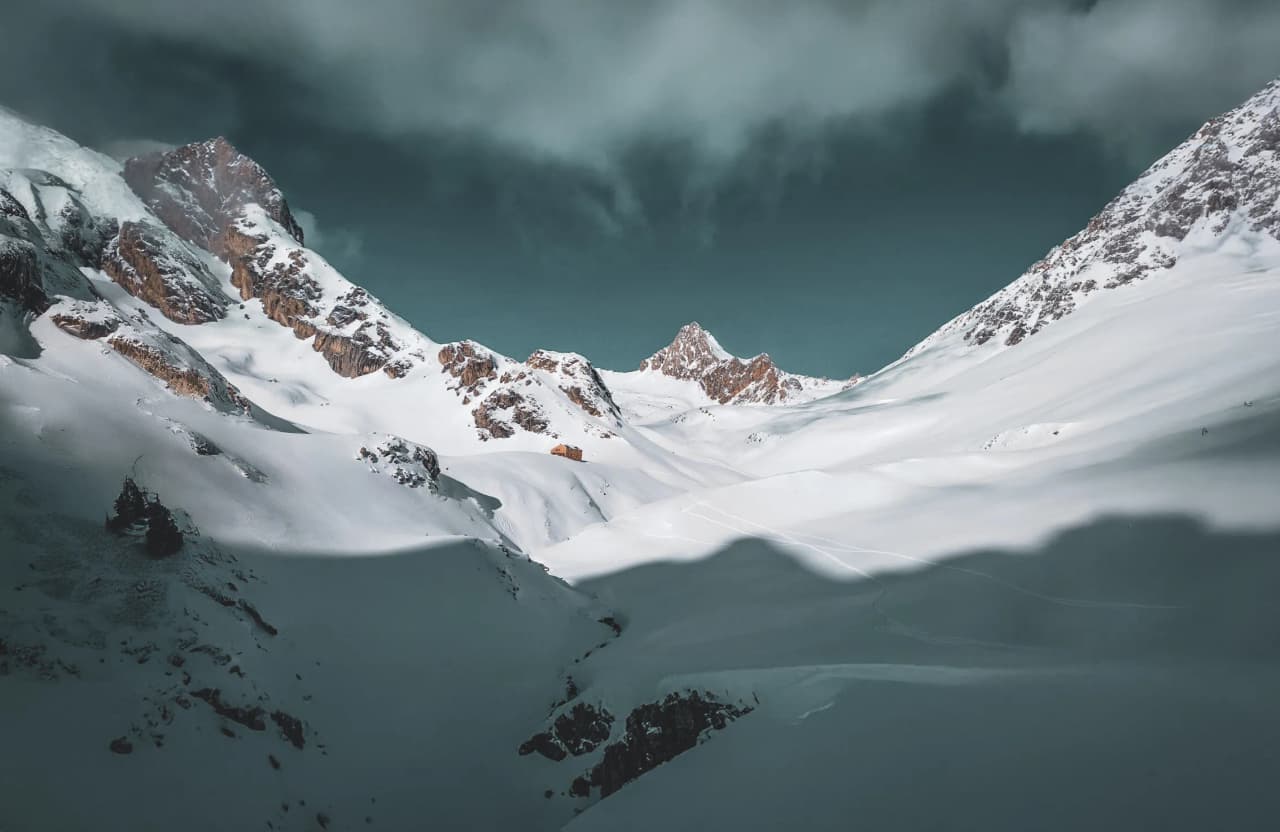 Paysage alpin majestueux, montagnes enneigées et ciel dramatique, invitation à l'aventure.