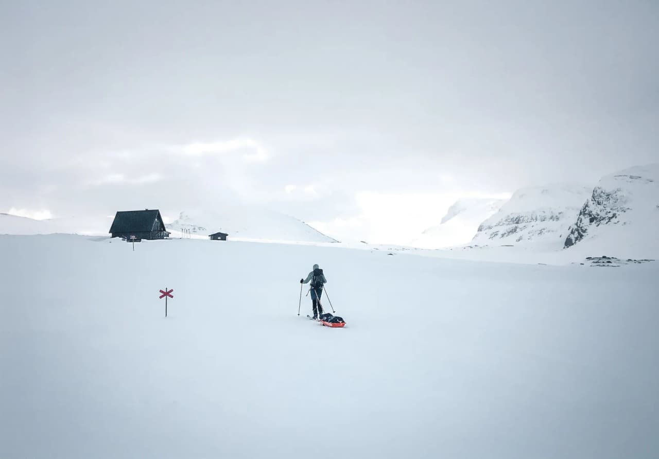 Een skiër doorkruist een uitgestrekt besneeuwd landschap in Lapland, tegenover geïsoleerde Berghutten.