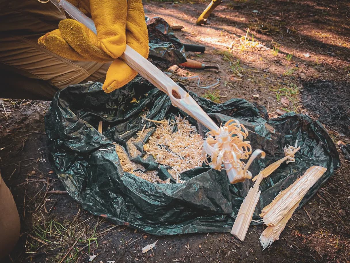 Een deelnemer aan een survivalcursus boetseert hout in het bos en ontdekt de kunst van het overleven.