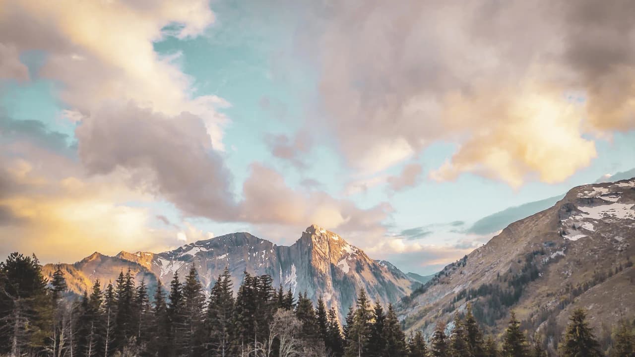 The mountain landscape of the Hautes Bauges, with sun-drenched peaks, lush green forests and vibrant skies.