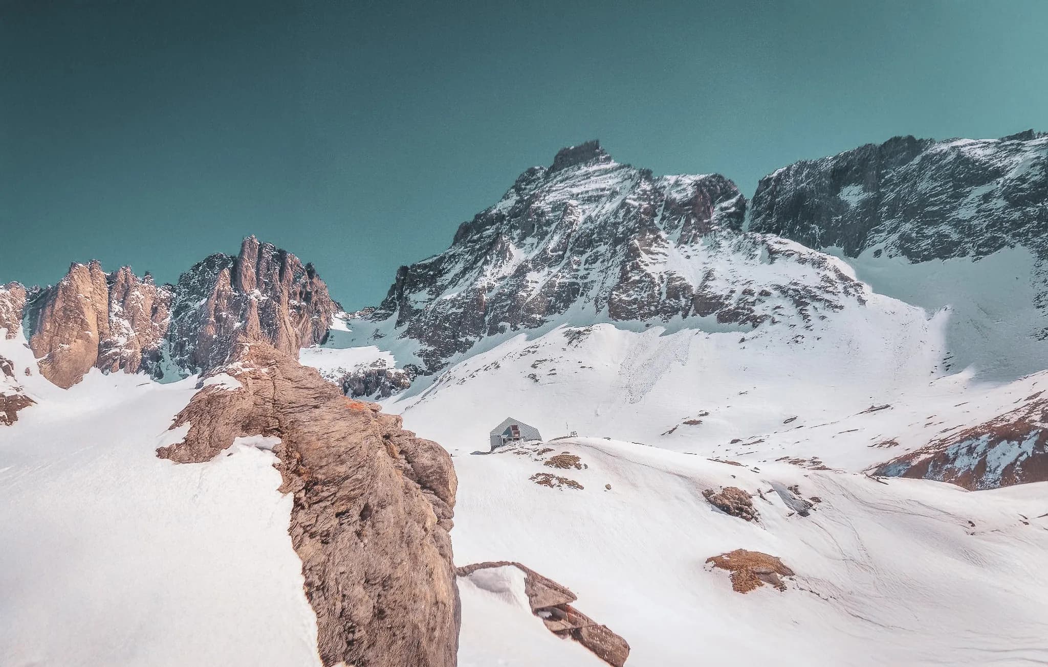Un paysage alpin majestueux, avec des montagnes enneigées et un refuge isolé.