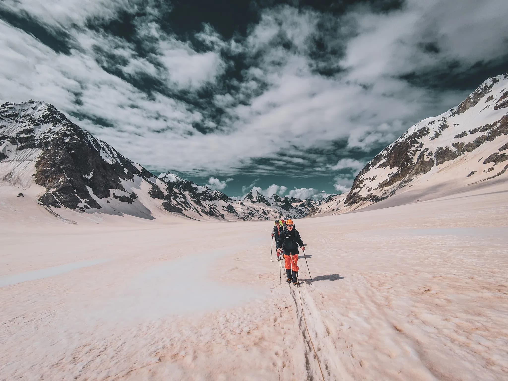 A group of hikers cross a magnificent glacier under cloudy skies in the Alps.