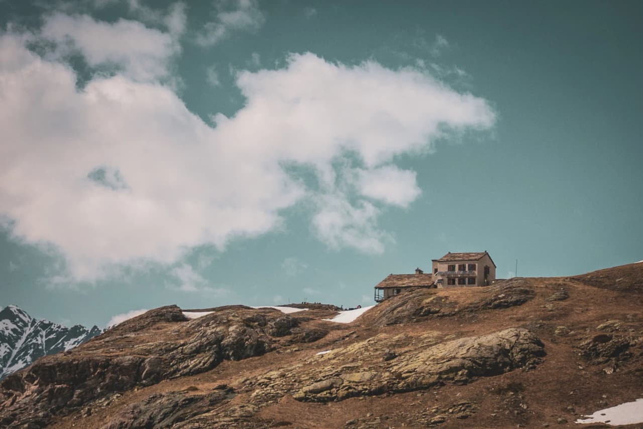 A picturesque mountain hut surrounded by majestic mountains and blue skies.