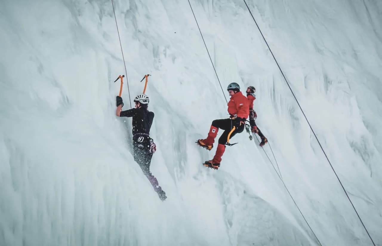 Trois alpinistes escaladent une cascade de glace dans les Alpes italiennes, paysages éblouissants.