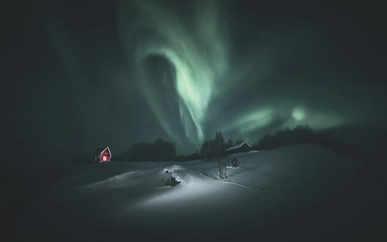 Sublime aurora borealis illuminating a snow-covered landscape, with traditional houses in the background.