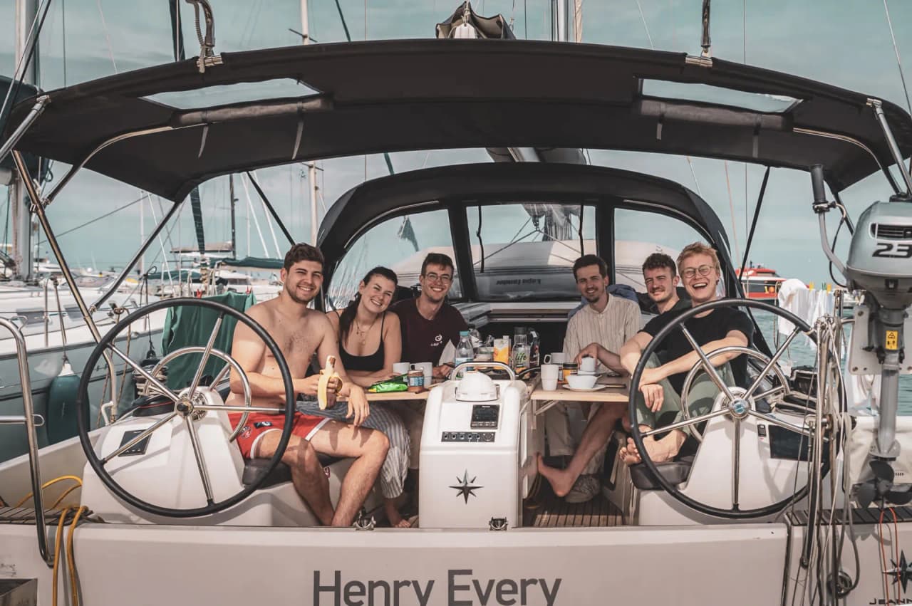 Cinq amis souriants partagent un moment convivial à bord d'un voilier en Méditerranée.