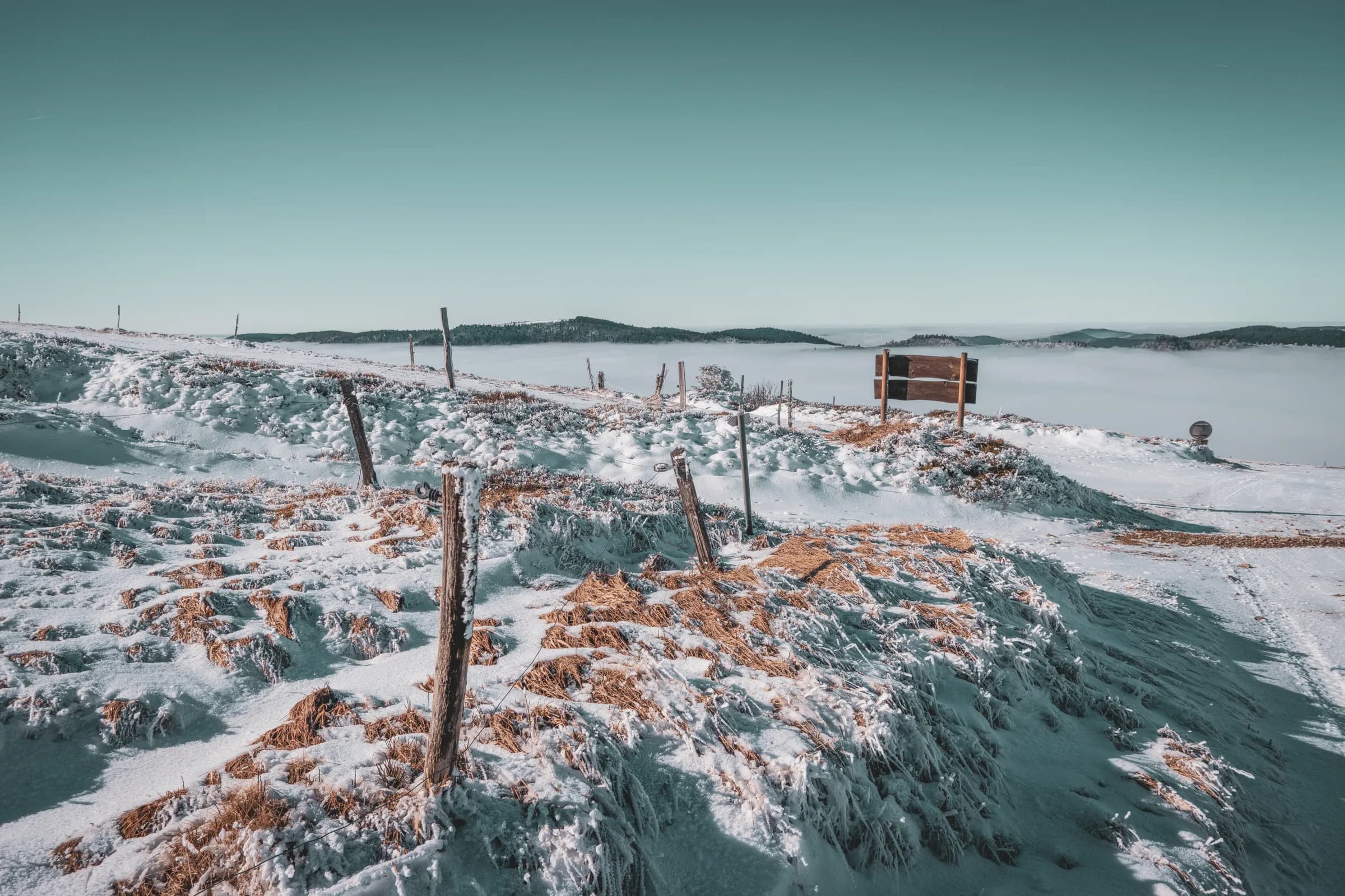 A snowy landscape with rolling hills covered in a fine layer of snow. Wooden posts, probably fences, stand here and there, adding a touch of rusticity to the landscape.