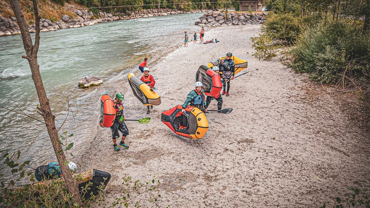 Een groep mensen in packrafts aan de oever van een rivier, die samen genieten van een gezellig moment midden in de natuur.