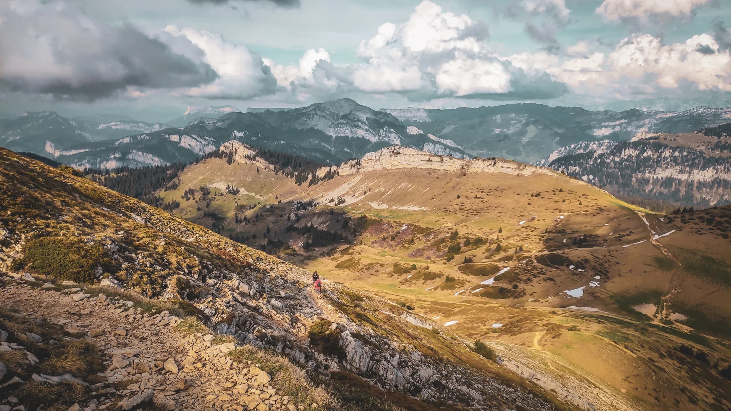 Randonneuse marchant sur un sentier escarpé, entourée de paysages montagneux majestueux.