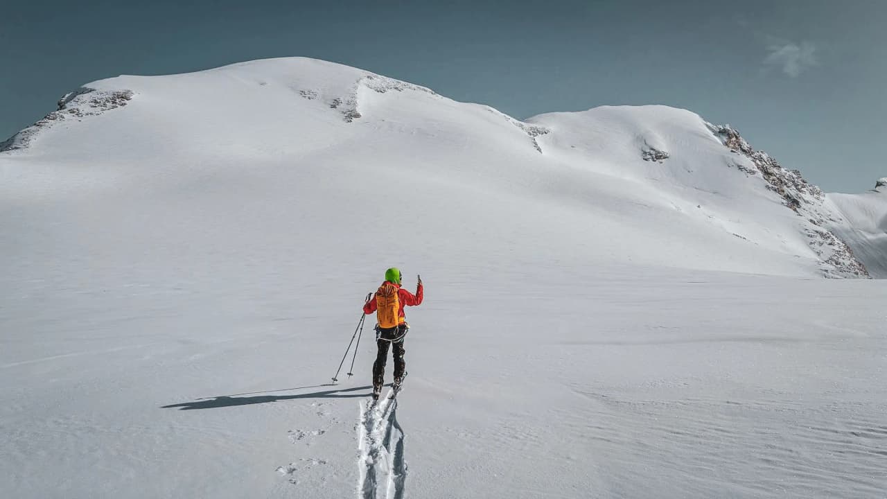 A skier traversing a snow-covered alpine landscape, between majestic peaks and sparkling glaciers.