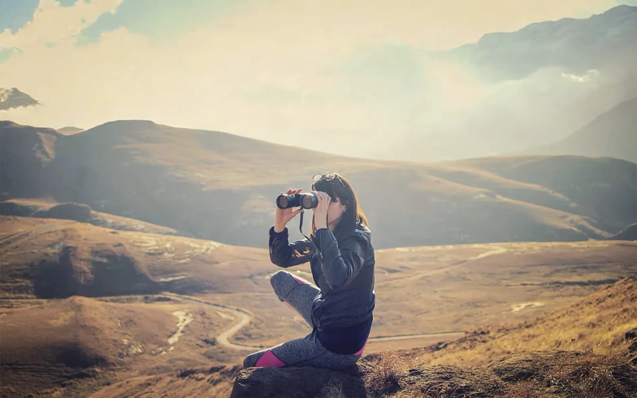 A traveller on a rock, observing the wildlife of the Écrins with binoculars.