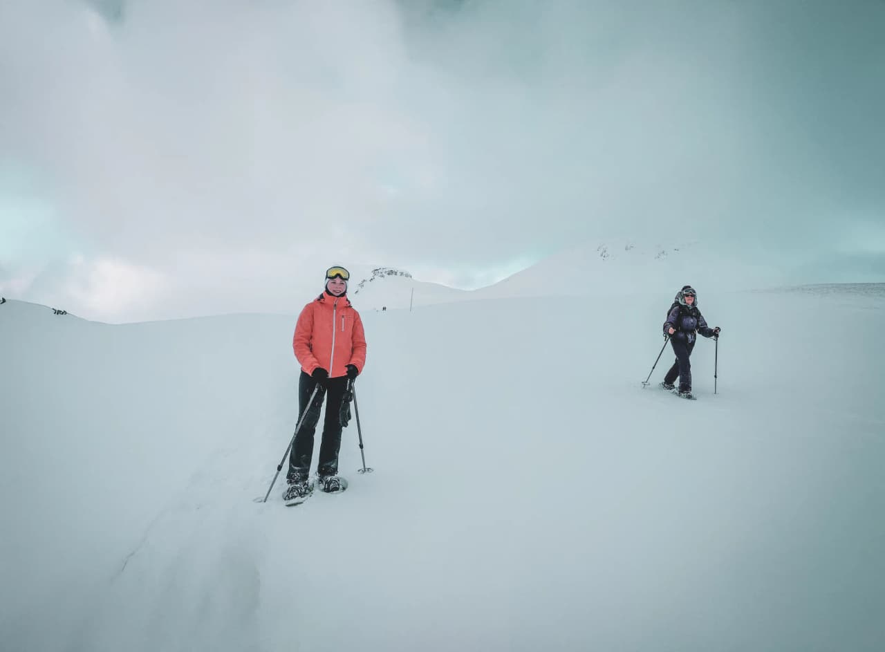 Two hikers on snowshoes, surrounded by sparkling snow, under a cloudy sky in Lapland.