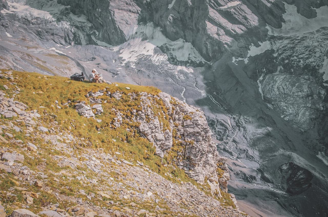 A hiker sitting on a green slope, admiring the majestic mountains and glaciers of the Alps.