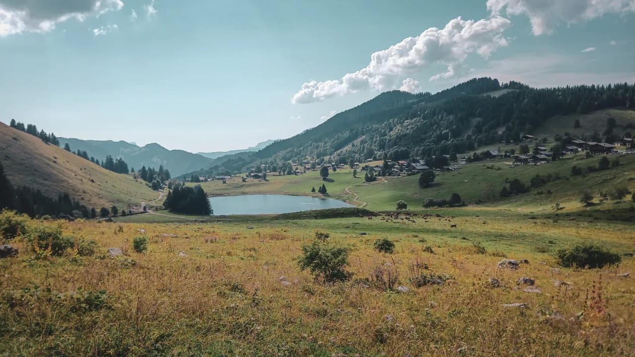 Een vredig meer omringd door groene bergen en zonnige bergweiden, een uitnodiging om te ontsnappen.