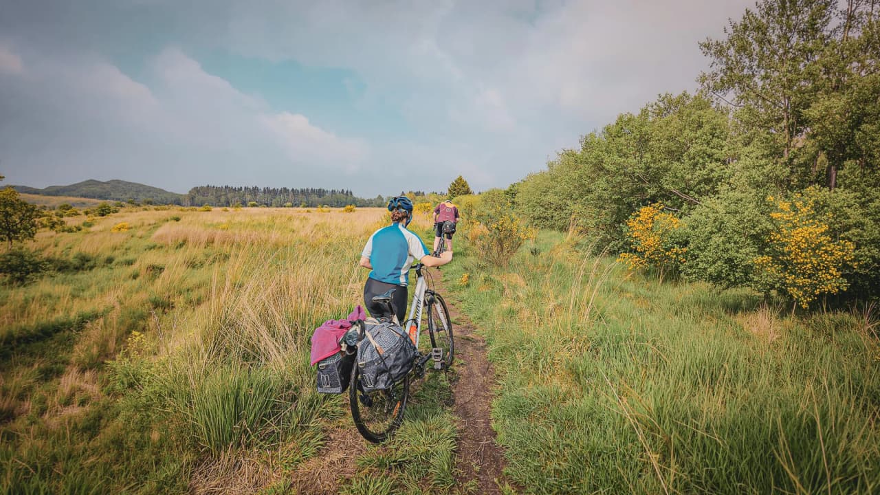 Twee fietsers verkennen de Hoge Venen, omgeven door groen en bloemen. Een avontuur in de natuur!