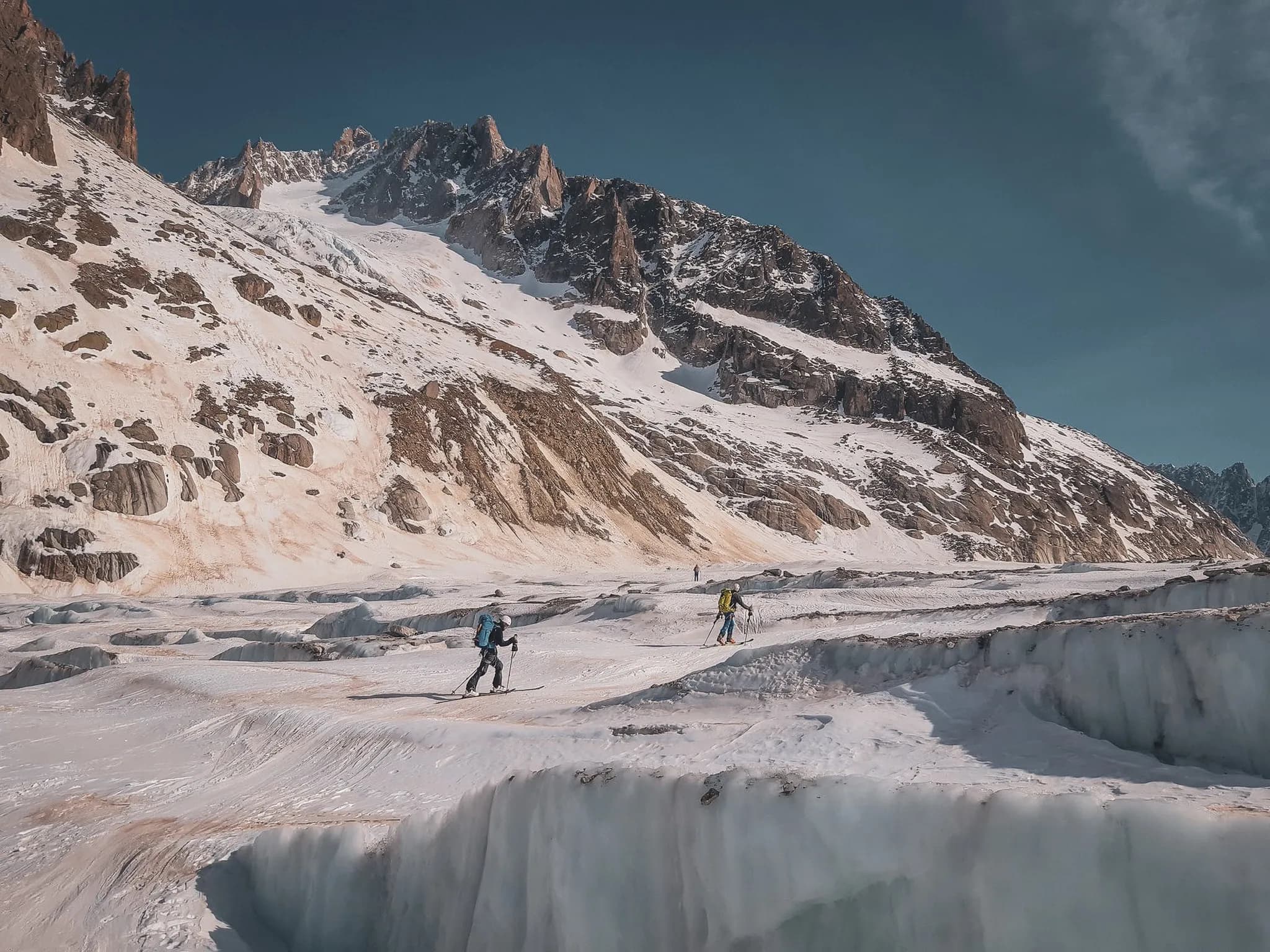 Skiërs die een gletsjer oversteken onder majestueuze bergen, een uitnodiging voor alpien avontuur.