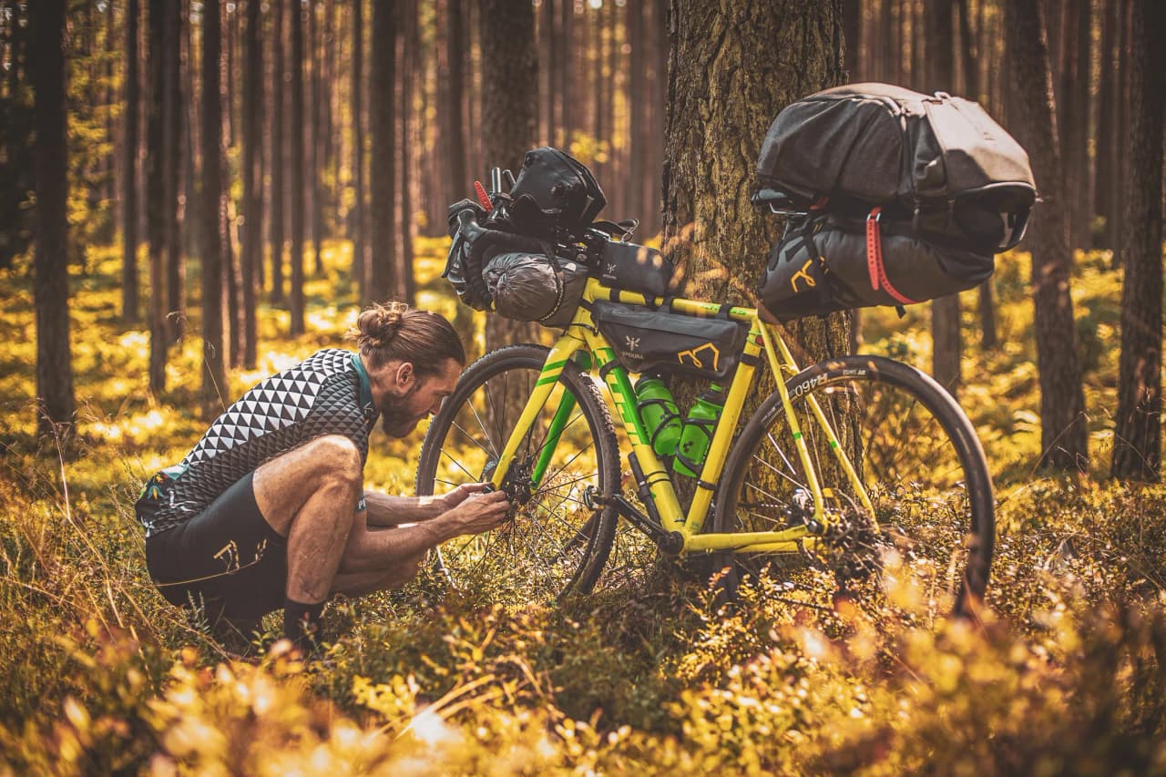 Cycliste en pleine nature, répare son vélo au cœur des forêts ardennaises, lumière dorée.