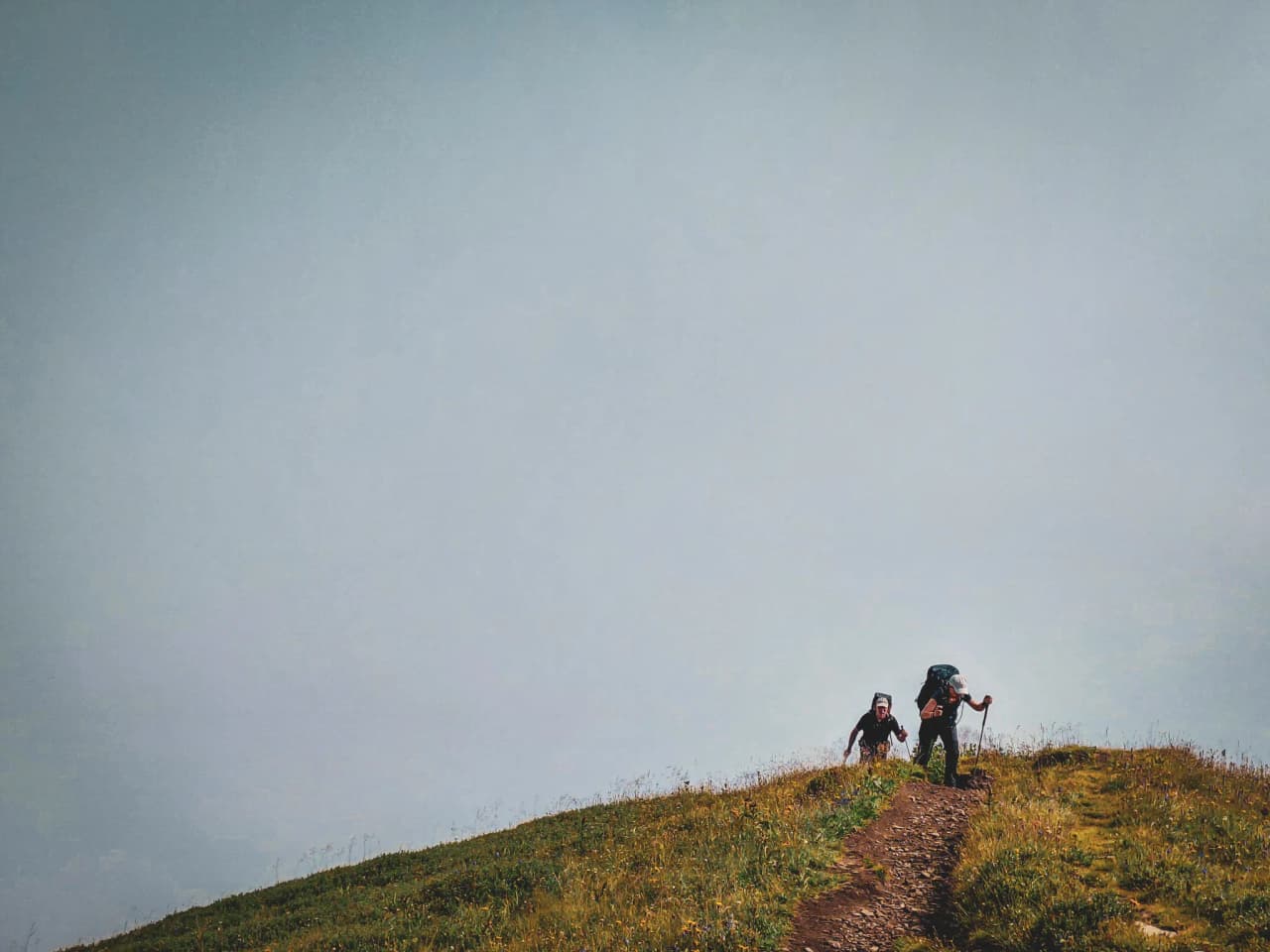 Two hikers climb a green path under cloudy skies in the heart of the Alps.