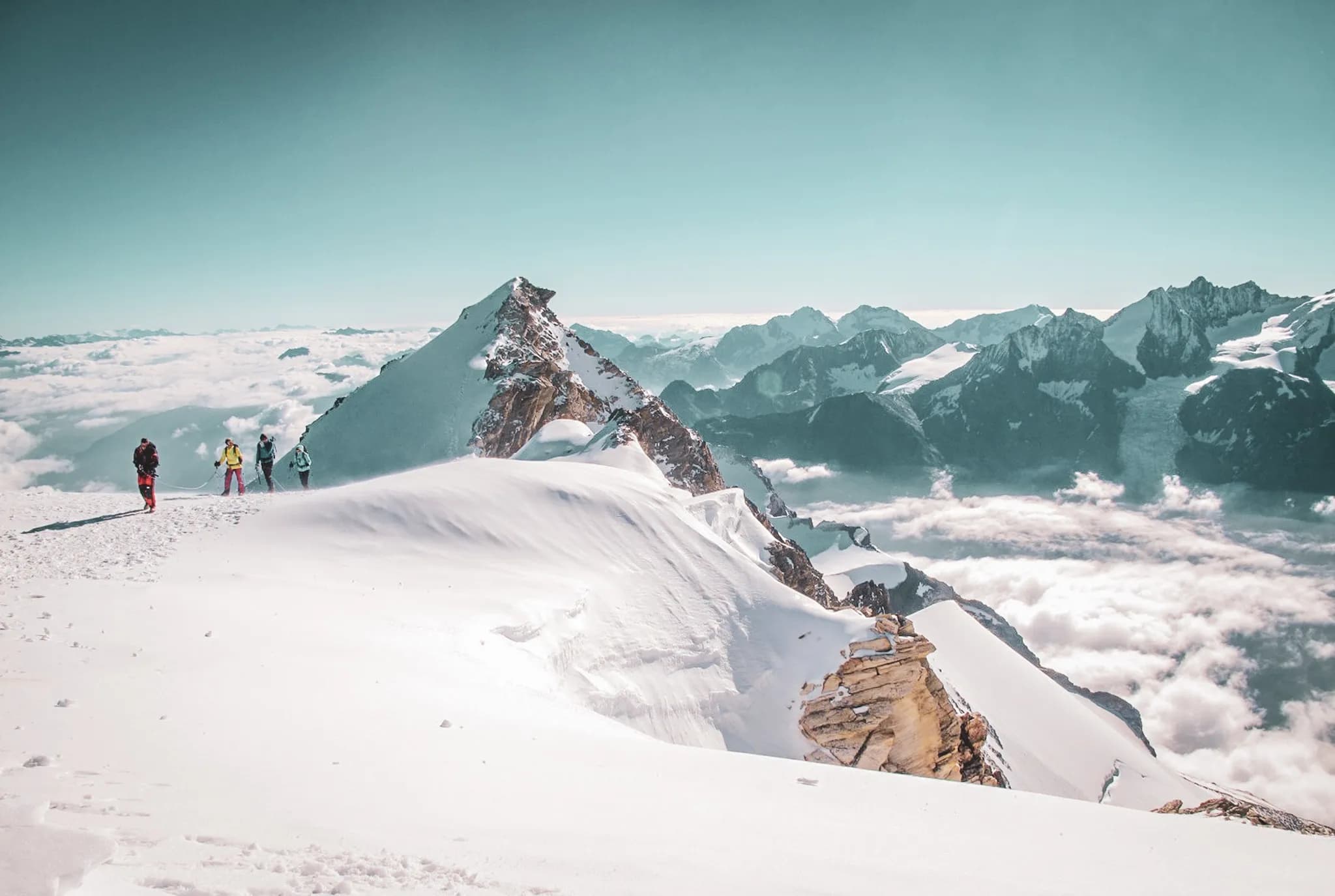 A group of climbers on a snow-covered summit, with stunning panoramic views of the Swiss Alps.