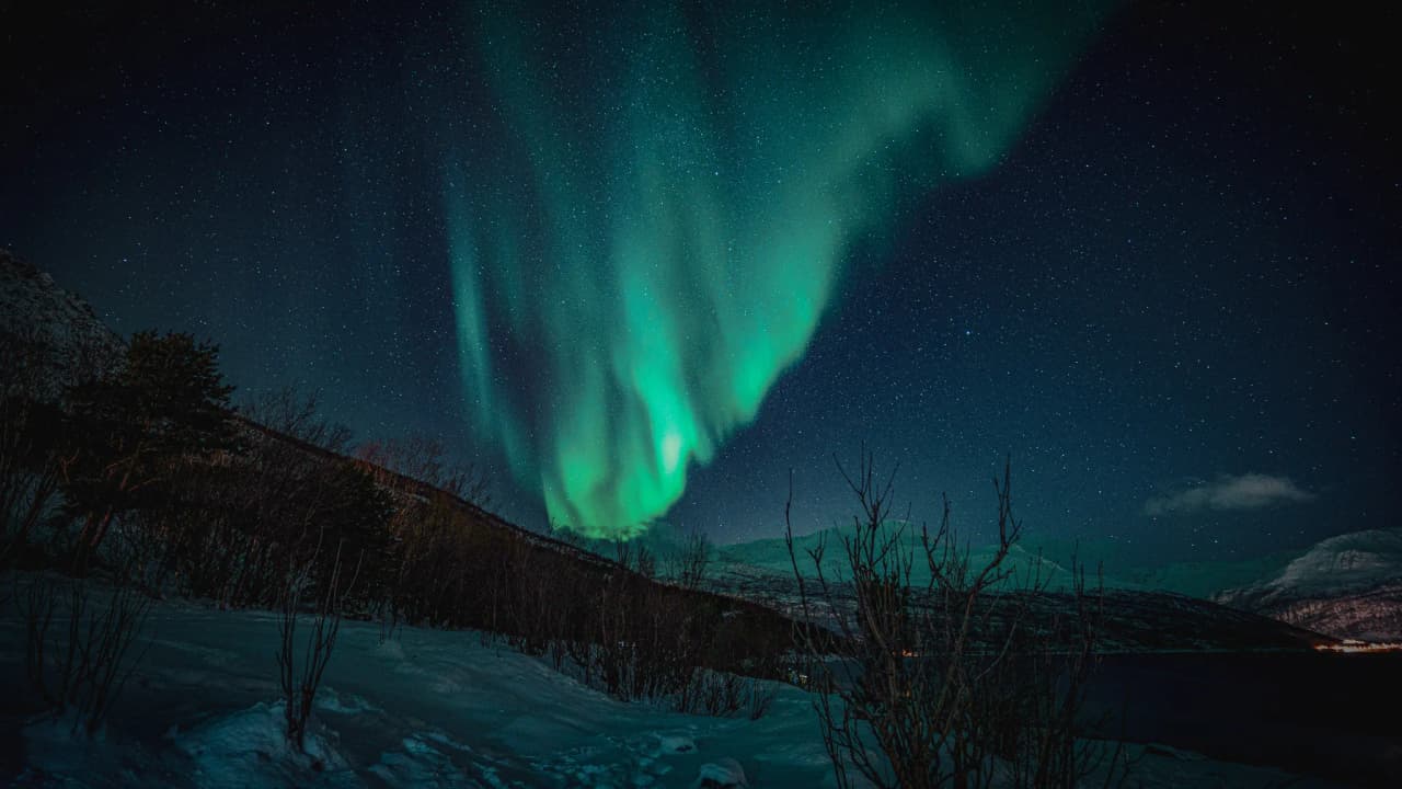 The Northern Lights against a starry sky over the snow-covered fjords of Tromsø, Norway.
