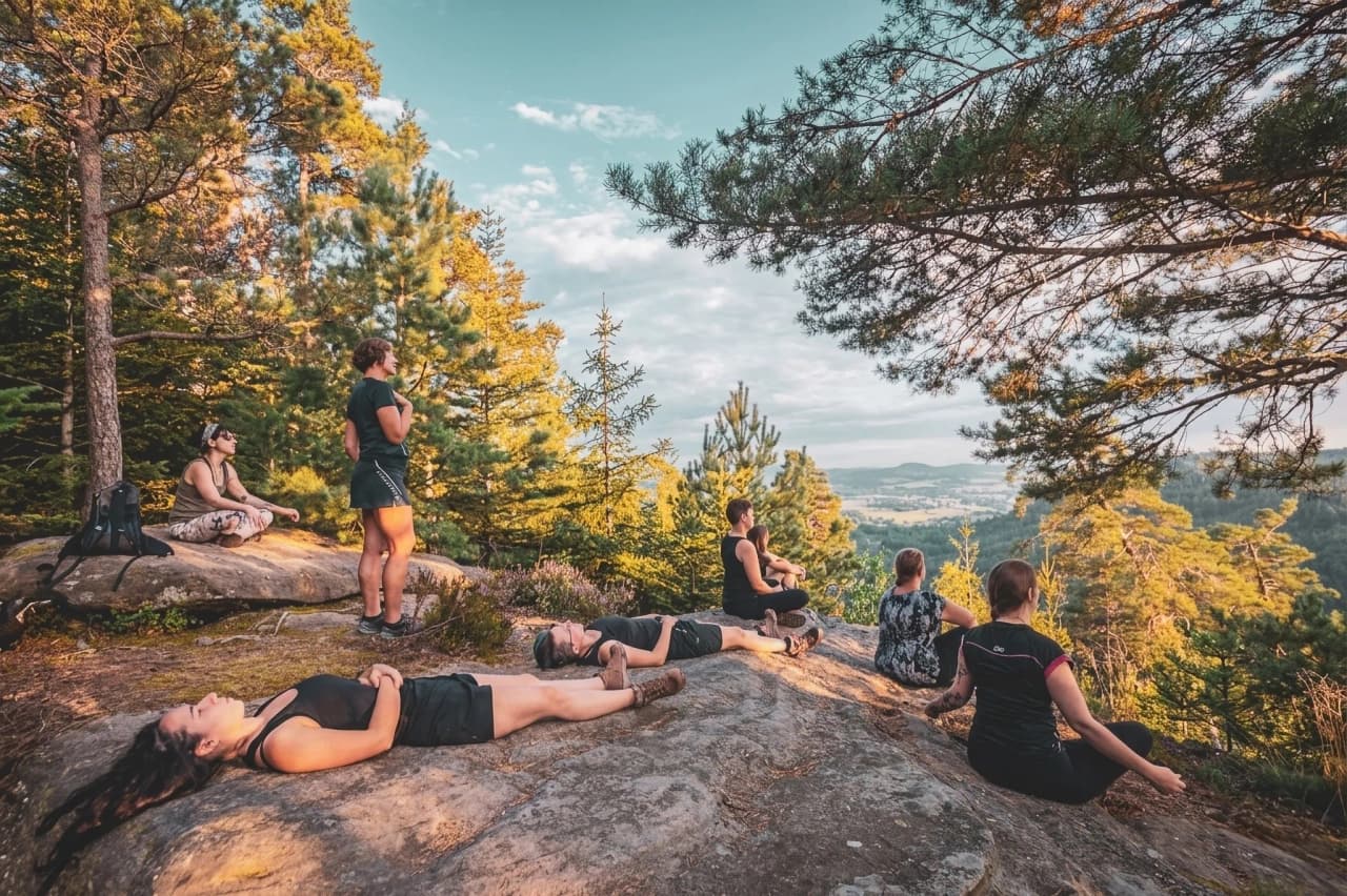 Een groep mensen mediteert op rotsen, omringd door weelderig groen bij zonsondergang.
