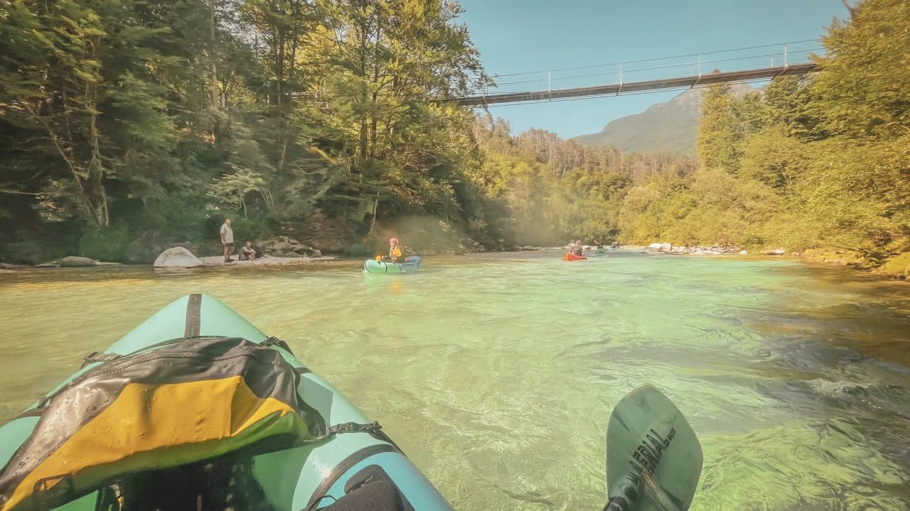 Three packrafts glide over crystal-clear waters, surrounded by greenery and sublime nature.