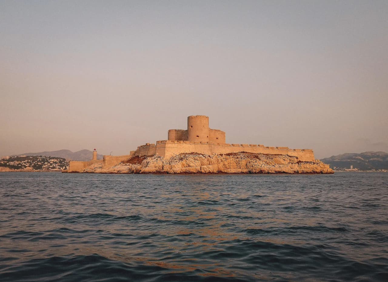 Château majestueux sur une île, entouré de mer turquoise et montagnes, evocat de l'aventure.