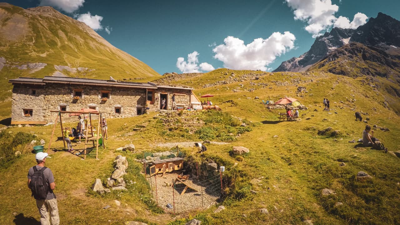 Refuge alpin pittoresque, entouré de montagnes verdoyantes et de familles en pleine nature.