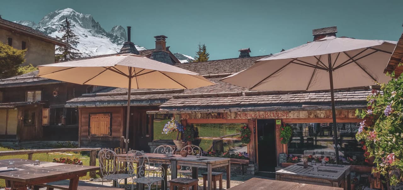 Auberge pittoresque en montagne, avec parasols et vue sur les sommets enneigés du Mont-Blanc.
