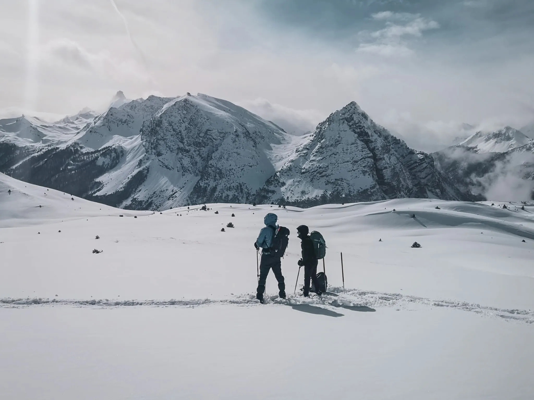 Two hikers on snowshoes in the heart of a snow-covered Alpine landscape, surrounded by majestic mountains.