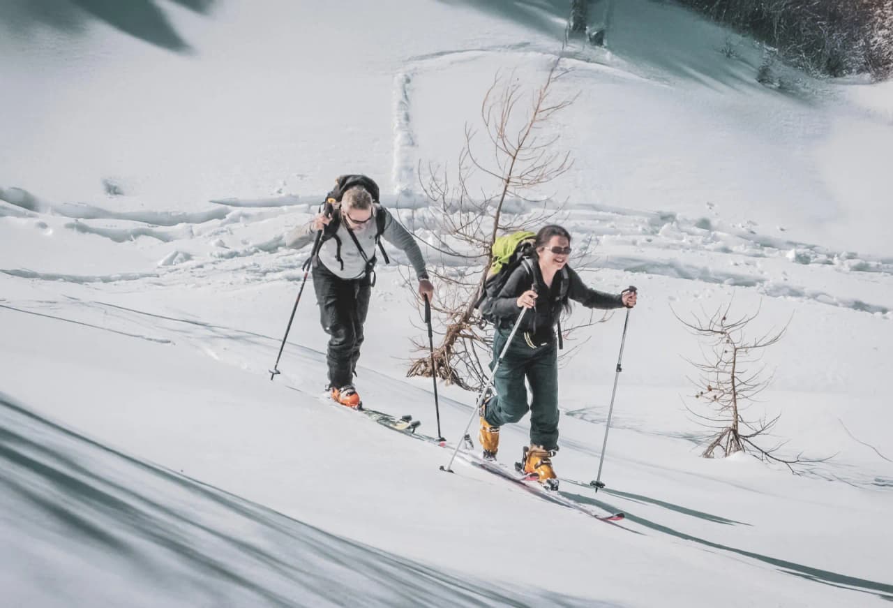 Deux skieurs progressent avec le sourire sur un terrain enneigé des Alpes italiennes.
