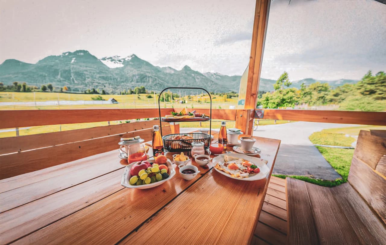 A room with welcoming green walls, featuring two wooden beds with circular-patterned sheets. There is a wooden cupboard with an illustration of horses hanging above it. To the right, a door leads