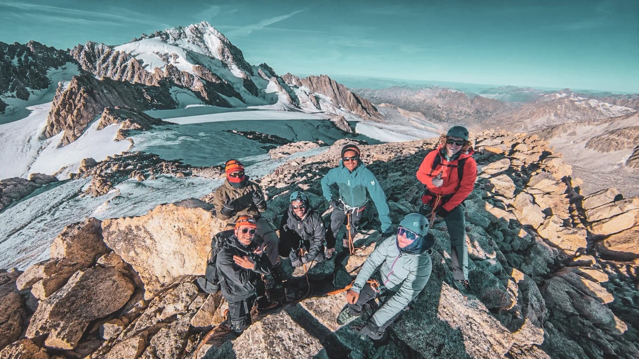 Groupe d'alpinistes souriants au sommet, avec des montagnes majestueuses en arrière-plan.