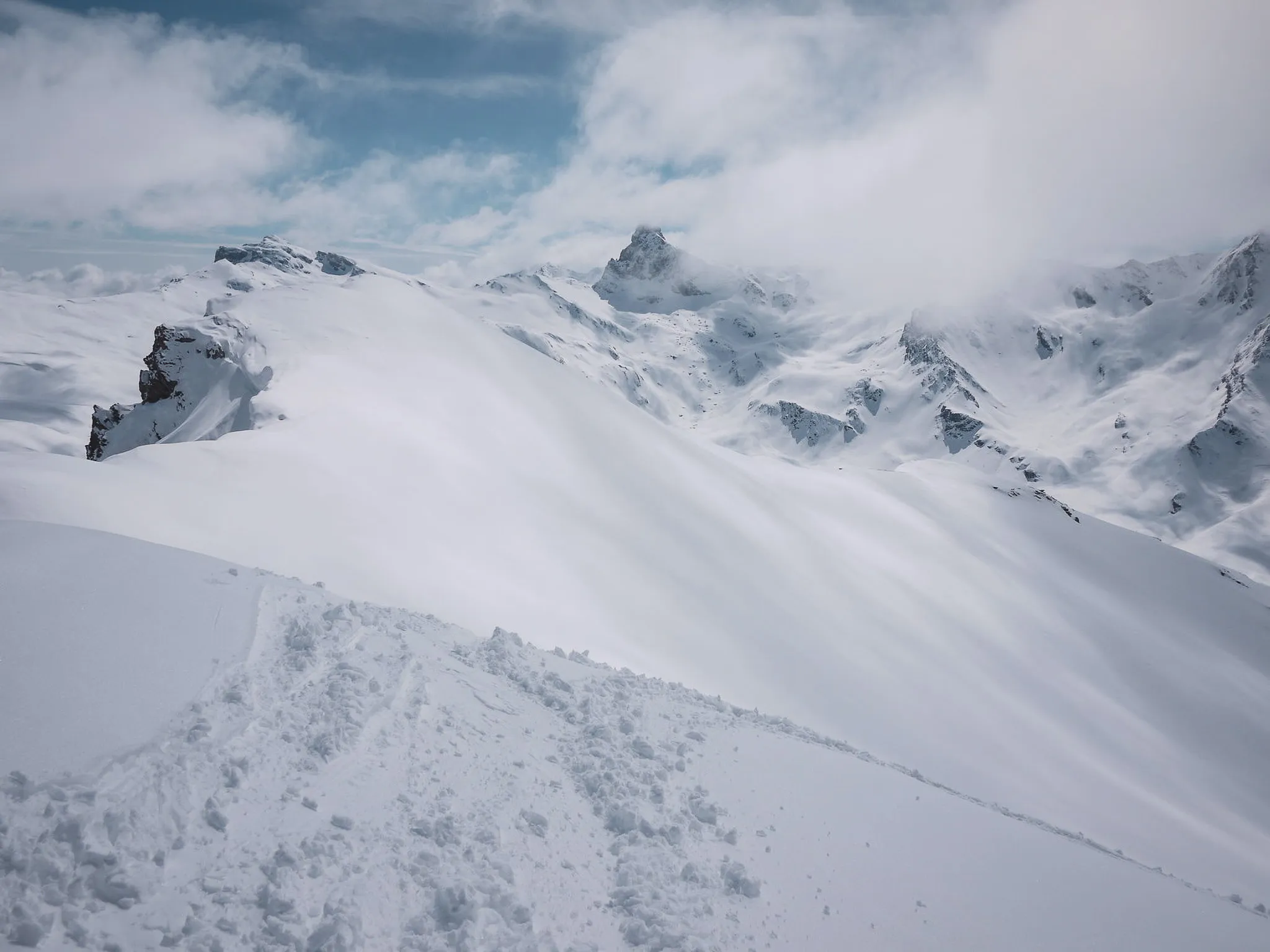 A breathtaking winter landscape of snow-capped peaks and blue skies dotted with clouds.