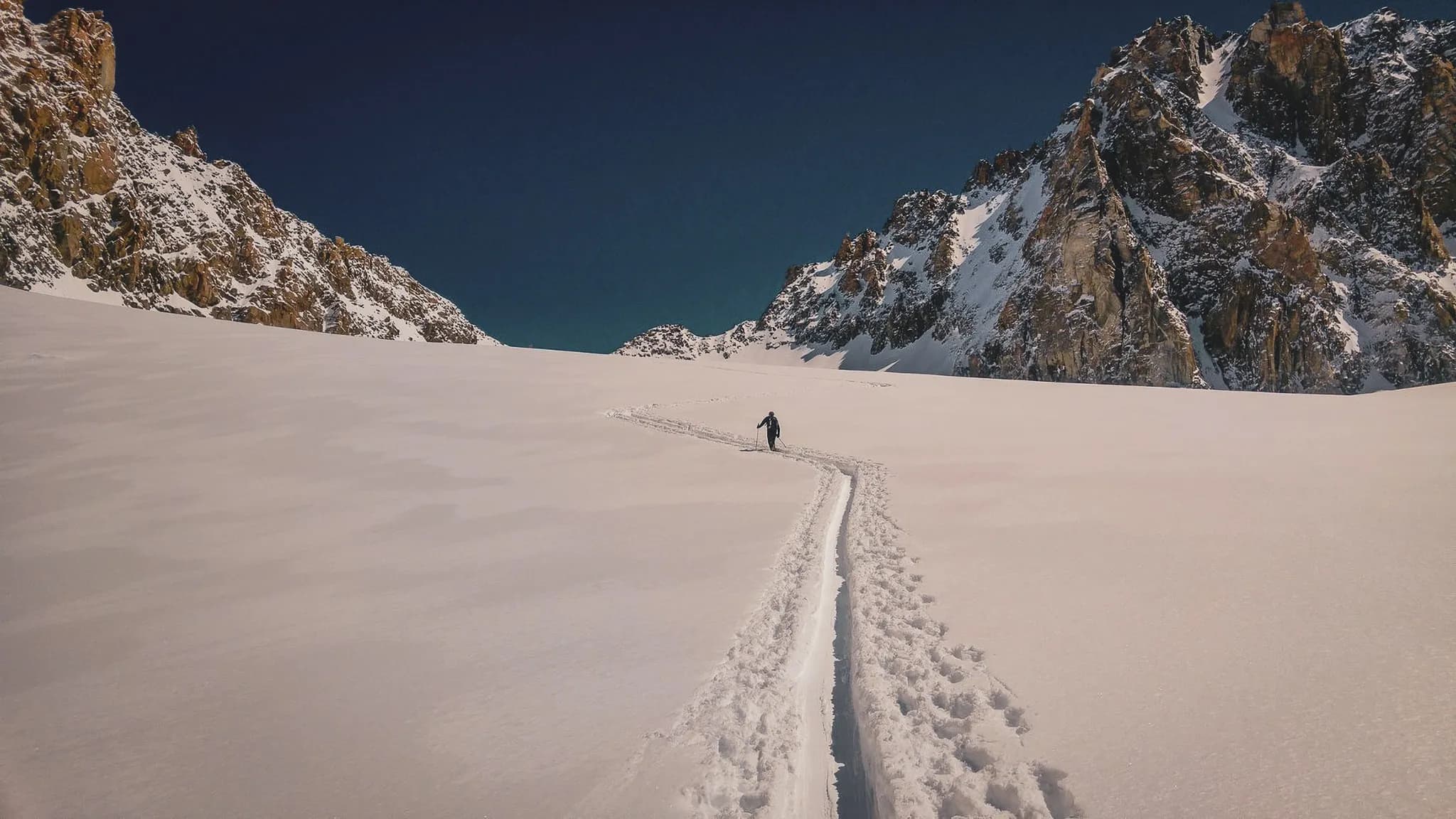 Een eenzame skiër baant zich een weg over een brede gletsjer onder een stralend blauwe hemel.