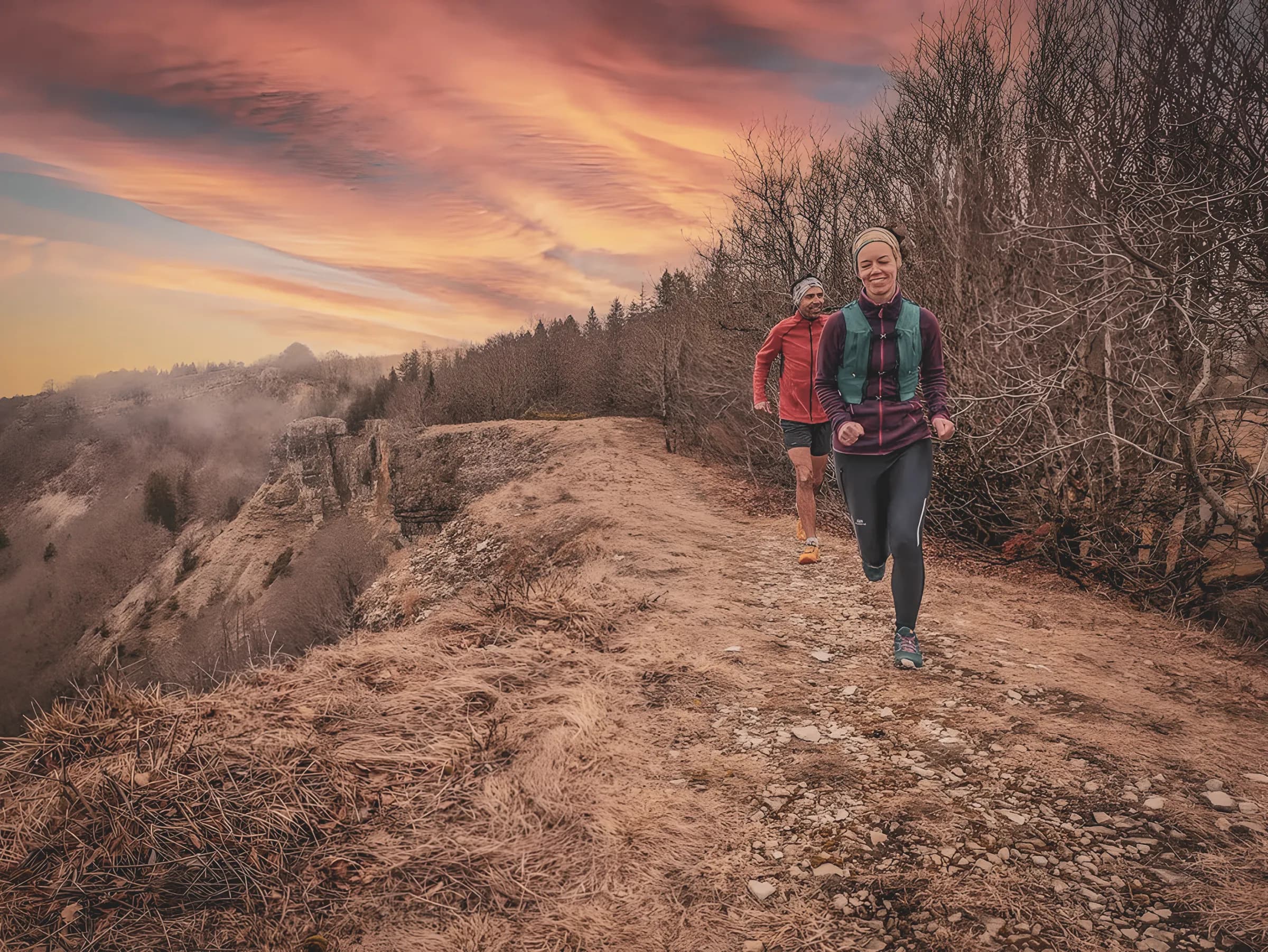 Couple courant sur un sentier montagneux, sous un ciel coloré au coucher du soleil.