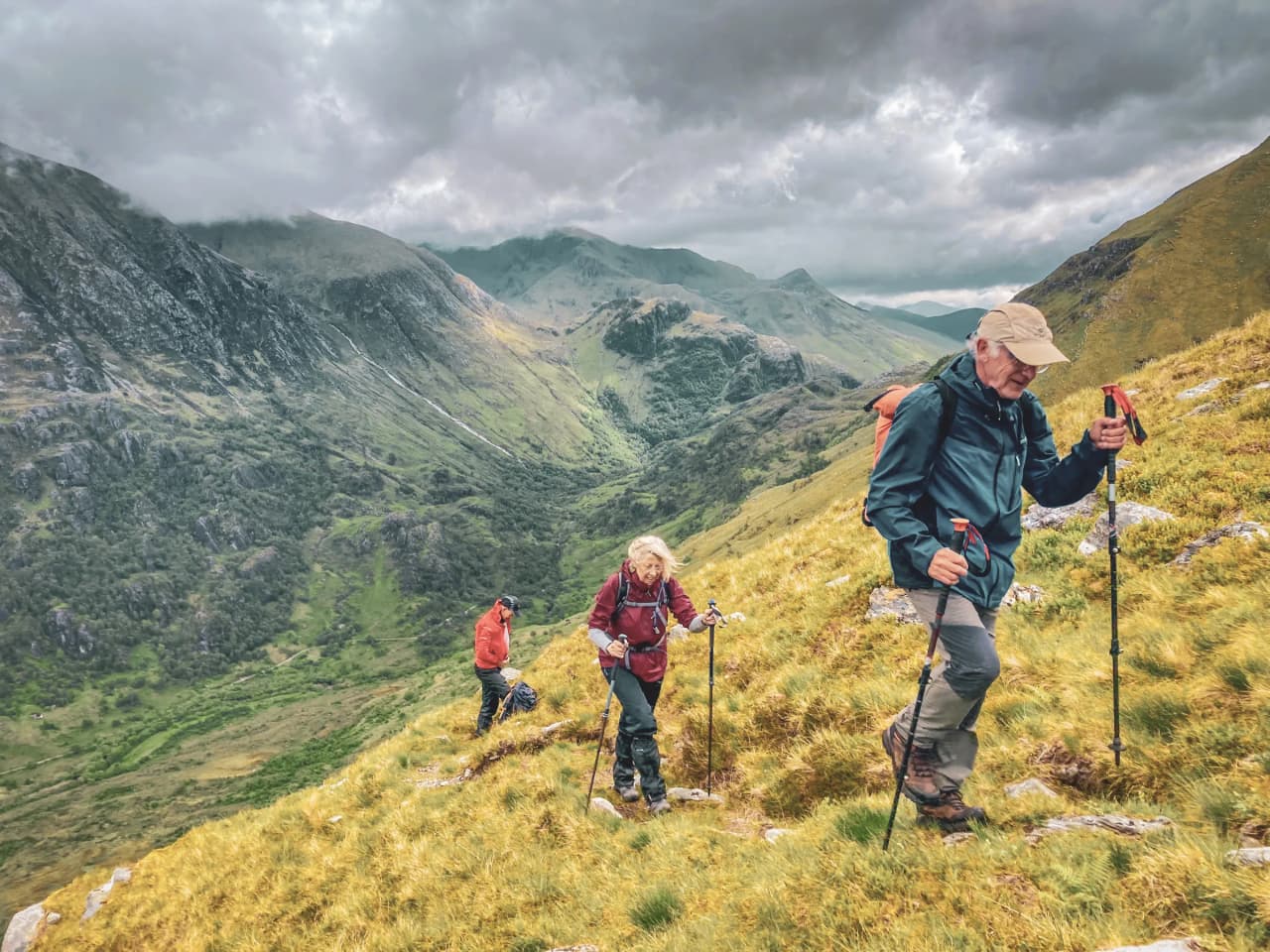 Hikers exploring the green hills of the Scottish Highlands under cloudy skies.