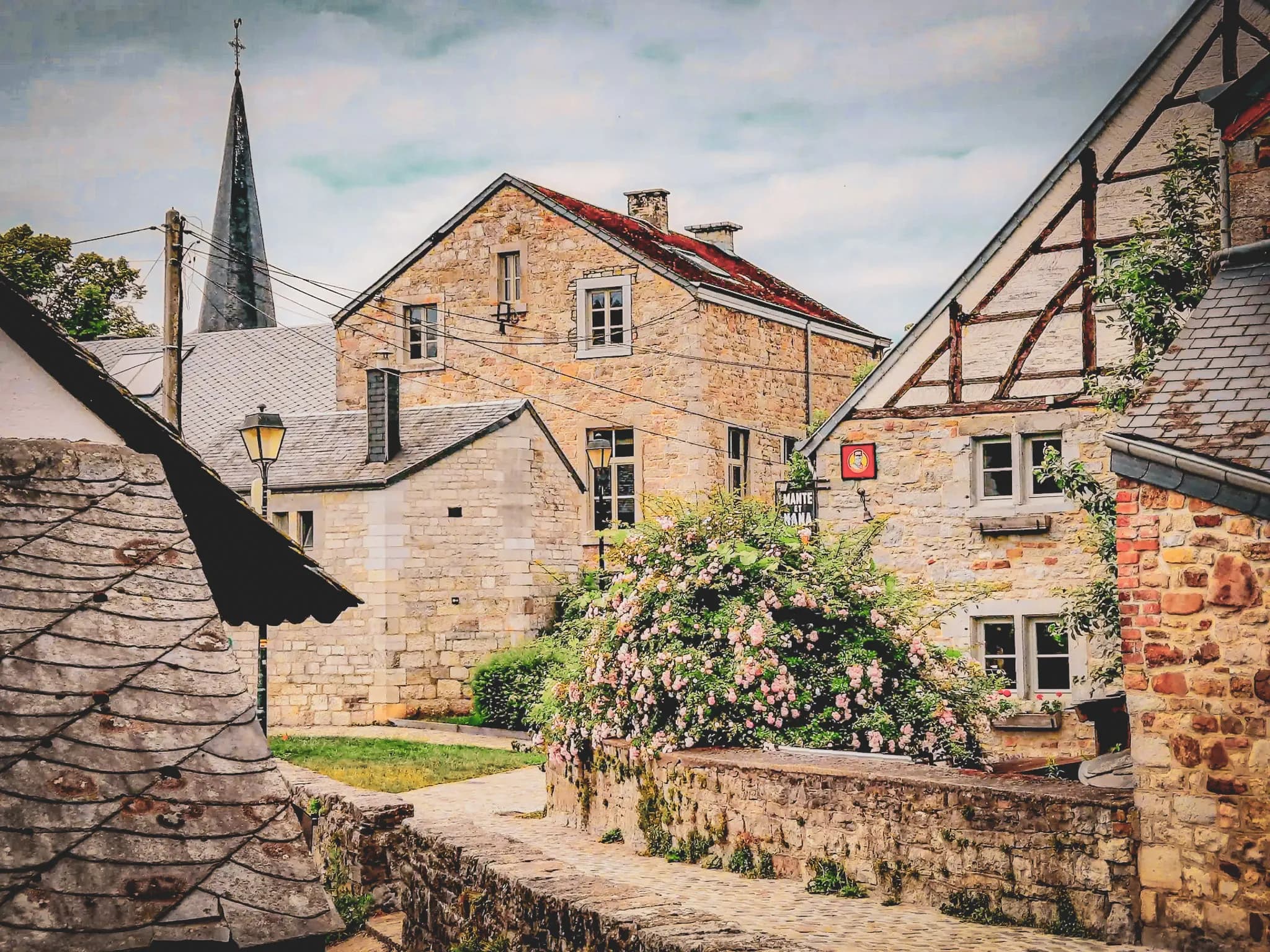 A picturesque village with stone houses and tiled roofs, nestling in the heart of nature. A church tower with a slender spire stands in the background. The ru