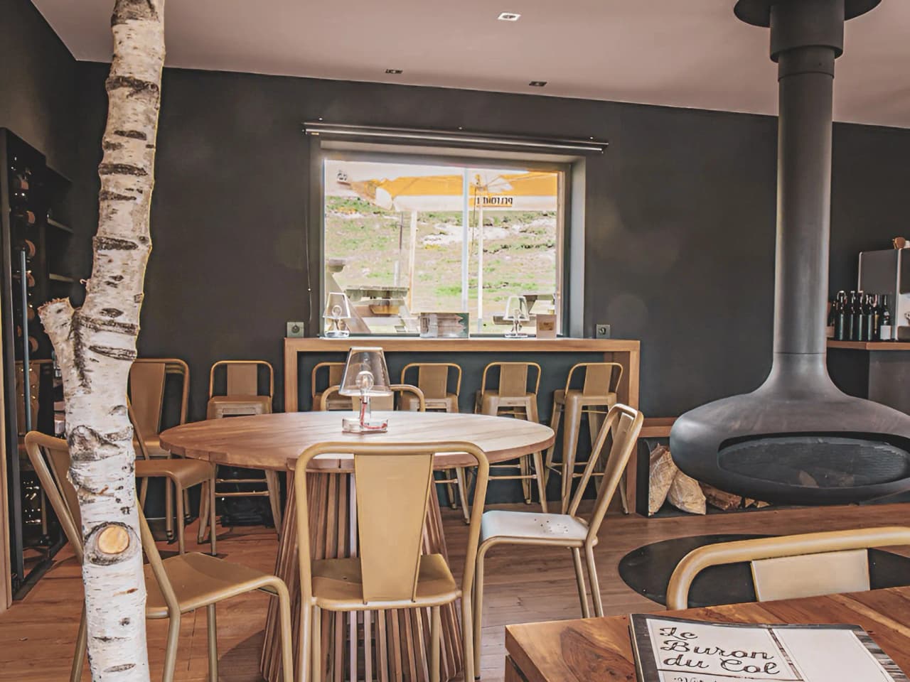 Un espace accueillant avec une table en bois, des chaises dorées et une vue sur la nature.
