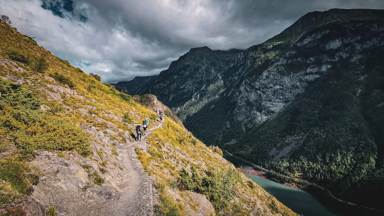 Sentier montagnard pittoresque avec randonneurs, vue sur des sommets majestueux et un lac.