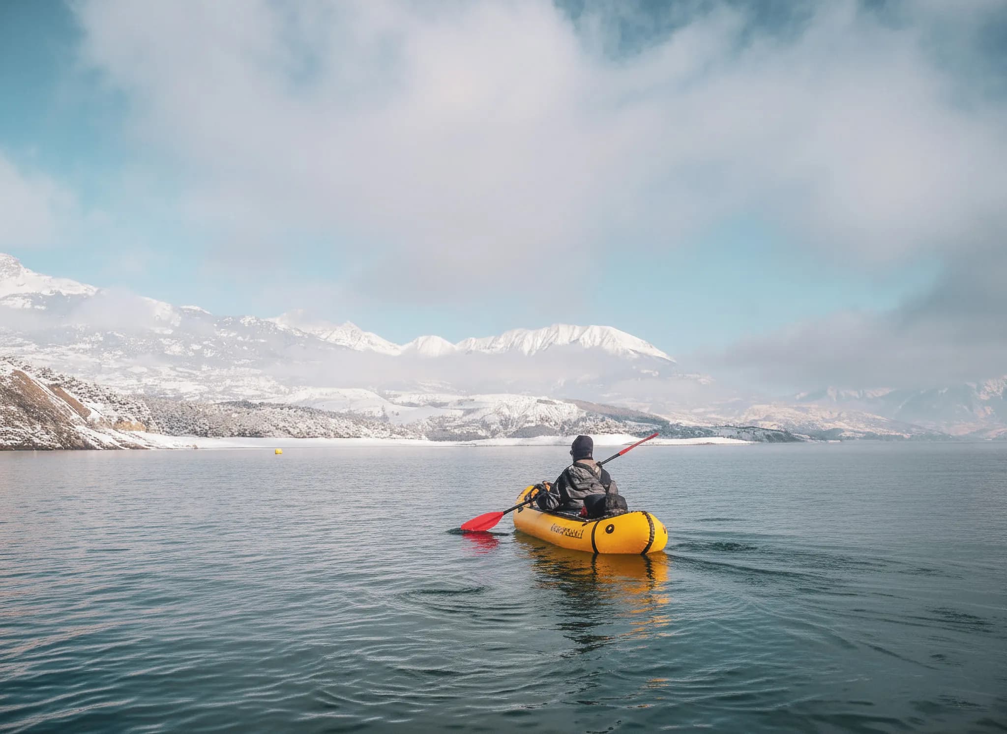 Un aventurier en packraft sur le lac de Serre-Ponçon, entouré de montagnes enneigées.