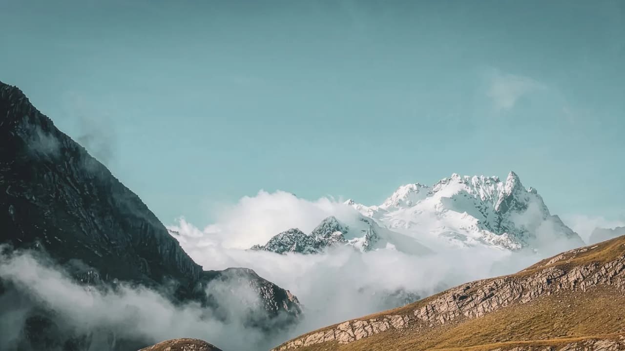 Paysage alpin majestueux avec des sommets enneigés émergeant des nuages, invitant à l'aventure.