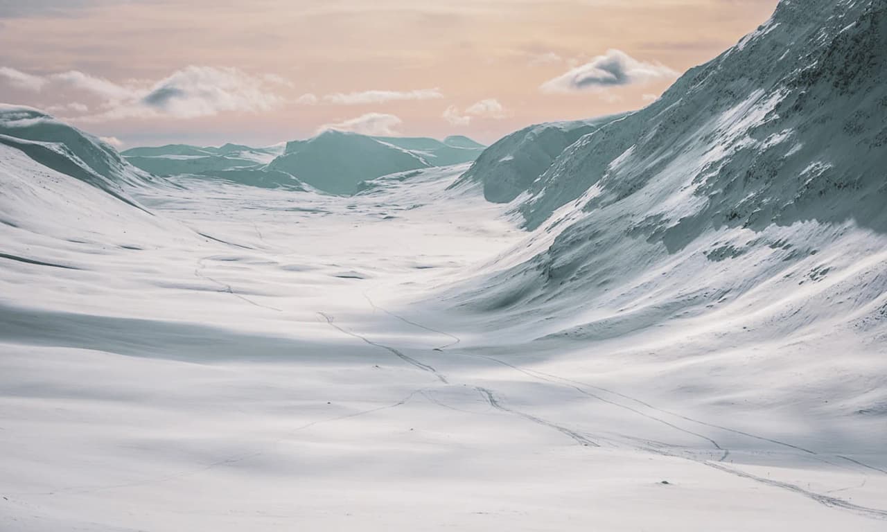 A vast snow-covered valley under a pastel sky, an invitation to escape to Swedish Lapland.