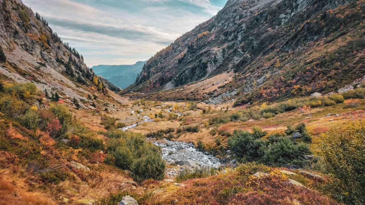 Een herfstkleurige bergvallei, met een kronkelend beekje en majestueuze bergtoppen.
