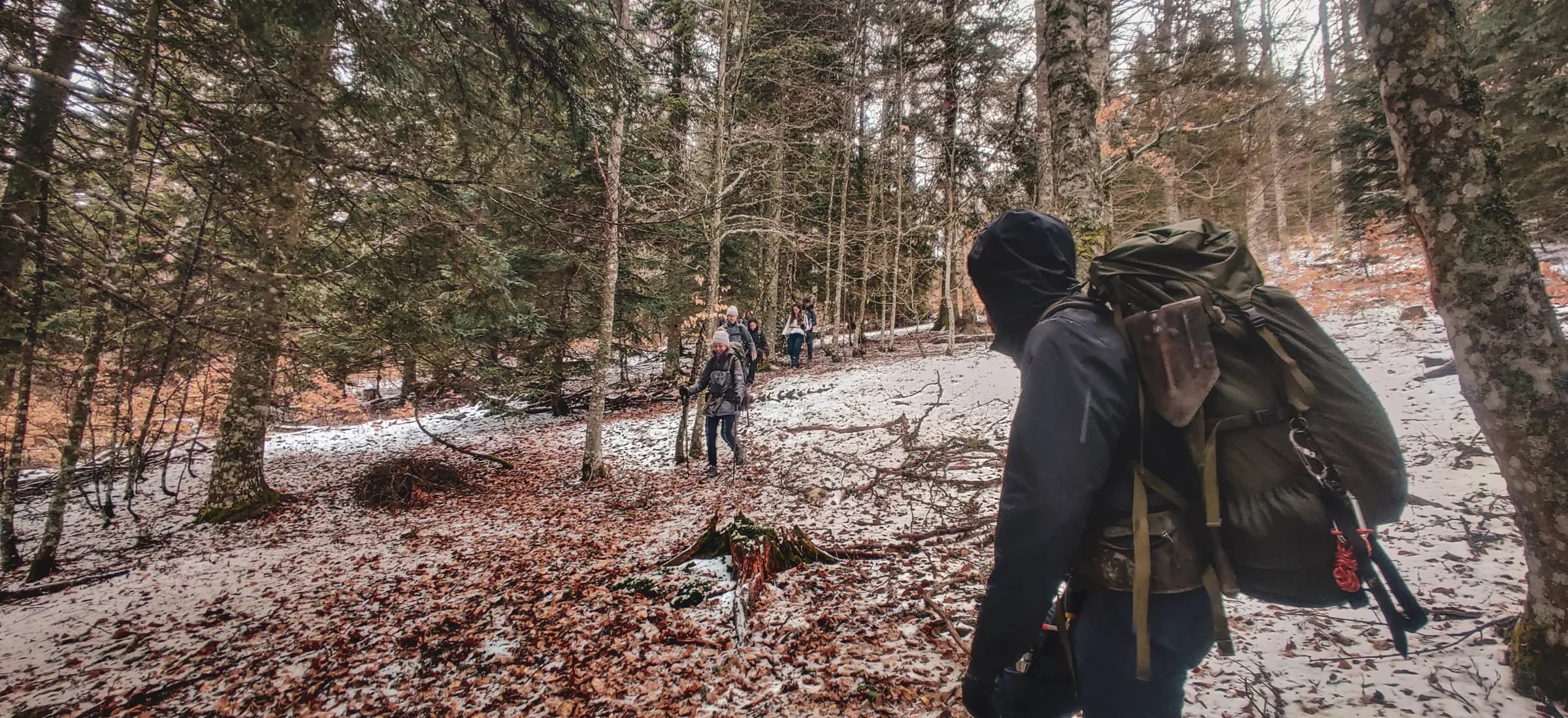 Een groep mensen in de natuur, wandelend over een bospad bezaaid met sneeuw en bladeren.
