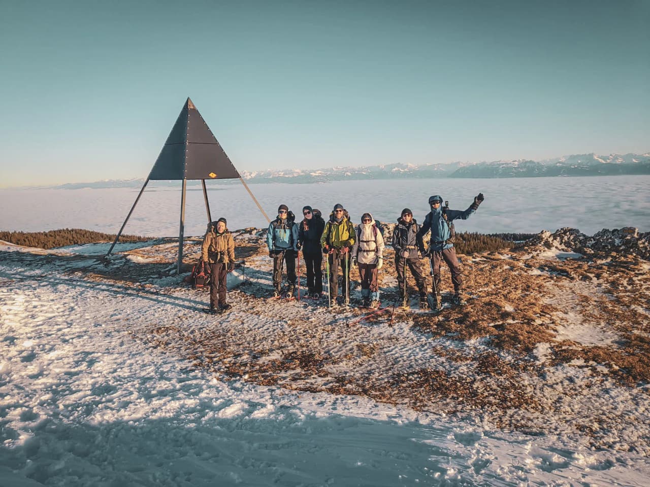 Groupe d'aventuriers en raquettes sur un sommet enneigé, panorama spectaculaire du Jura suisse.
