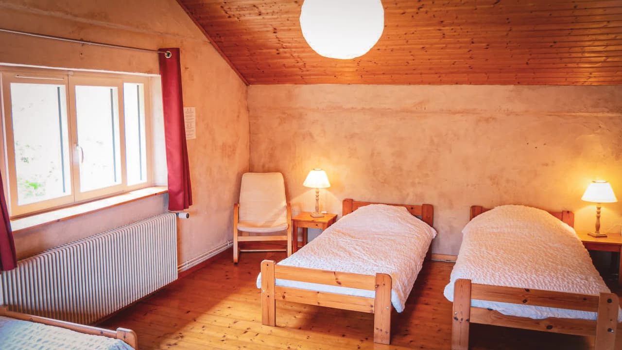A cosy wooden room with bright windows and twin beds, inviting you to relax.