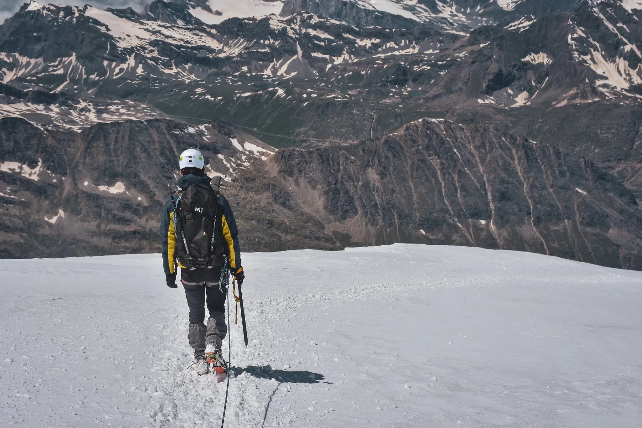 Een alpinist staat op de gletsjer van Gran Paradiso, gericht op het berglandschap. Gekleed in een gele jas en uitgerust met stijgijzers en een ijsbijl, zet hij zijn tocht voort.